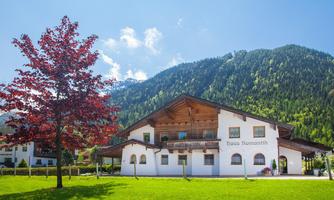 A charming house with a large garden and a clear blue sky. In the background, green mountains can be seen.