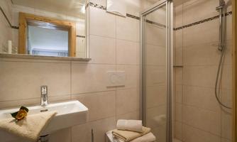 A modern bathroom with a shower and a sink. Clean towels are placed on a white surface, and a leaf with a flower decorates the room.