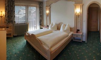 A cozy bedroom with two single beds and a wooden frame. The windows bring plenty of daylight into the room.