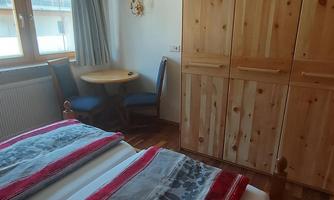 A cozy bedroom with two beds, wooden furniture, and a small table. The room has a window looking outside and a television on the wall.