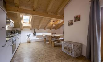 A modern kitchen with wooden ceilings and a large dining table. The room is bright and friendly with a wooden floor and windows.