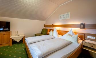A cozy bedroom with two beds and white pillows. There is a television on the wall and a green sofa.