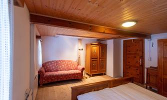 A cozy bedroom with a wooden floor and a wooden ceiling. A red sofa and a wooden piece of furniture are also in the room.