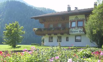 A charming house with traditional architecture and a beautifully blooming garden. In the background are gentle hills and trees.