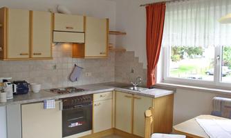 A modern kitchen with beige-white cabinets and a large window. The table is simply set and accommodates several people.