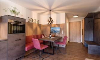 A modern, cozy living kitchen with a dining table and pink chairs. The room has a warm atmosphere and stylish elements.