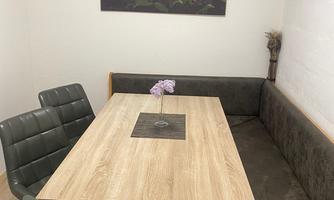A cozy dining area with a wooden table and an upholstered bench. A painting of colorful flowers hangs on the wall.
