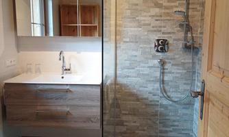 A modern shower with a glass partition and tiled walls. The floor is tiled, and a fresh green carpet complements the space.