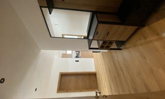 A bright entrance area with a wooden floor. On the left side, there is a shoe rack with a mirror and a coat hook.