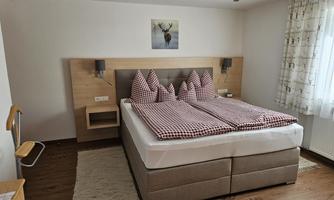 A modern bedroom with a large bed and checkered pillows. The decor is bright and cozy, complemented by wooden and textile accents.