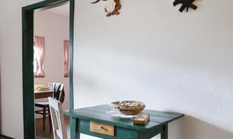 A simply furnished room with a green table and a chair. Antler trophies hang on the wall, and a door leads to another room.