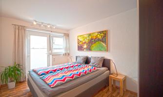 A cozy bedroom with a large bed and colorful bedding. There is a window looking outside and an appealing wall decoration.