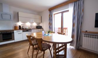 A modern kitchen with a round table and six chairs. The window offers a view outside and the decor is bright and friendly.