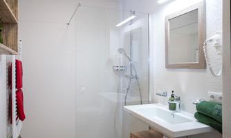 A modern bathroom with a glass shower and a sink. The design is simple and bright, featuring a mirror and a towel rack.