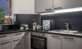 A modern kitchen with black and gray cabinets. On the countertop, there are cookware, plants, and a coffee capsule machine.