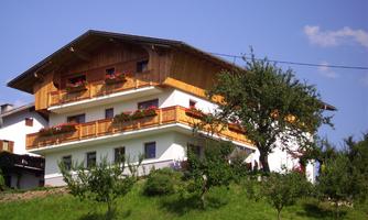 A traditional wooden house with a balcony and blooming flowers. Surrounded by green meadows and trees.