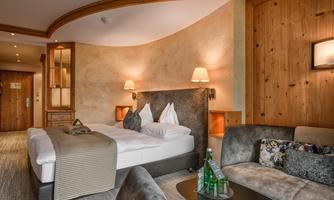 A cozy hotel room with a large bed and modern furnishings. Soft lighting and wooden details create a warm atmosphere.