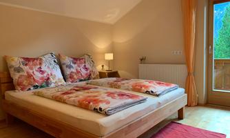 A cozy bedroom with a large bed and colorful bedding. A green view is visible through the window.