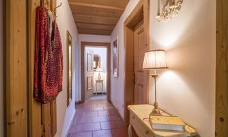 A bright hallway with wood details and cozy lamp light. Colorful textiles hang on the wall, and there is a beautiful dresser at the end of the hallway.