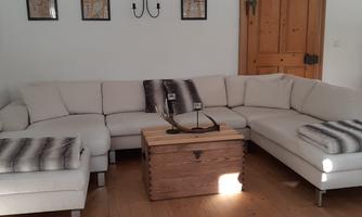 A modern living room with a large, bright corner sofa and a wooden table. On the wall hang some pictures, and the floor is made of wood.