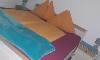 A cozy bedroom with a double bed and colorful cushions. An artwork hangs on the wall, and there is a nightstand as well as a colorful bedspread.