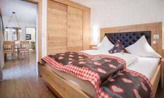 A cozy bedroom with a large bed and a wooden design. In the background, there is a dining area with wooden furniture.