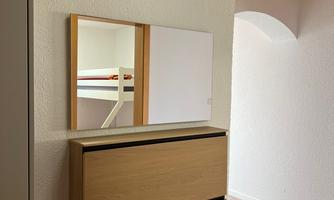 A modern hallway with a wooden cabinet and a mirror. The walls are light and the floor is made of wood.