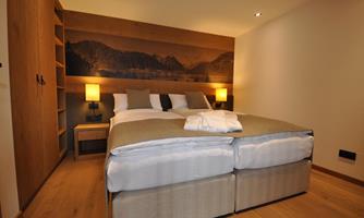 A modern bedroom with a large bed and cozy furnishings. In the background, there is an appealing wall decoration.