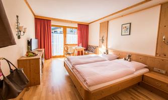 A cozy room with two beds and wooden furniture. The room has a balcony and is well lit.