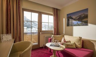 A cozy room with a red sofa and a small table. Large windows offer a beautiful view of the mountains.