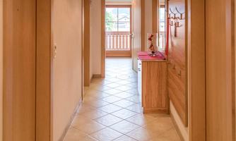 A bright hallway with wooden paneling and light tiles. On the sides, there are doors and a piece of furniture with a decoration.