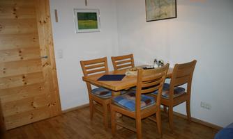 A cozy dining area with a wooden table and four chairs. The walls are light, and there are simple decorative elements.