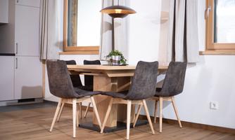 A modern dining area with a wooden table and chairs in a neutral color. Large windows let in plenty of daylight.