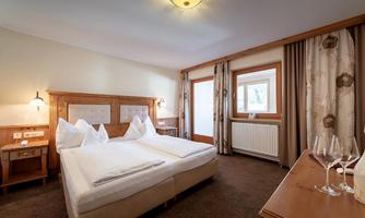 A cozy hotel room with a double bed and elegant wooden furniture. The room offers a view of the window and a peaceful atmosphere.