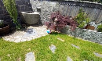 A small garden with a stone wall and low-maintenance plants. A round paved area and a water basin are also visible.