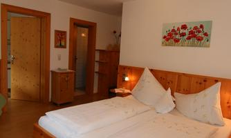 A cozy bedroom with a large double bed and wooden details. There is an open space with access to doors and a creative mural.