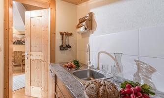 A cozy kitchen with wooden elements, a sink, and fresh vegetables. On the countertop lies a loaf of bread and some radishes.