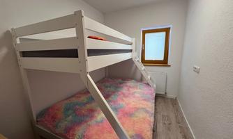 A cozy room with a bunk bed and colorful bedspreads. A window provides natural light.
