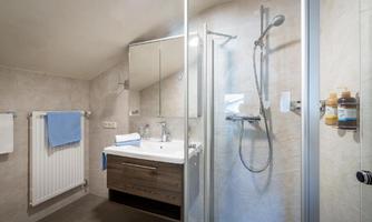 A modern bathroom with a glass shower cabin and a stylish sink. Towels hang on the wall and there is a heating system.