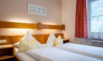 A cozy bedroom with two single beds and soft furnishings. The walls are painted in gentle colors and there are curtains with a floral pattern.