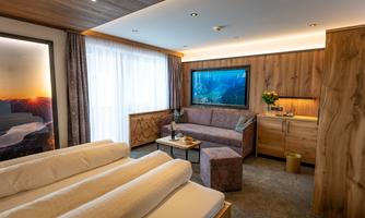 A cozy room with a double bed and a seating area. A large television and windows provide plenty of daylight.