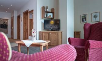 A cozy room with red armchairs and a wooden table. There is a TV on the wall and there are decorative pictures.