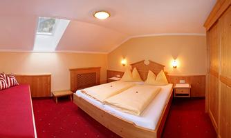 A cozy bedroom with a double bed and wooden furniture. The walls are in warm colors, and there is daylight through a window.