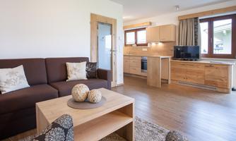 A modern living room with a cozy sofa and a wooden table. The open kitchen is well-equipped and plenty of light creates an inviting atmosphere.