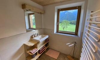 A modern bathroom with wooden ceilings and a large window.  
The sink area is designed in a minimalist style and offers a view of the green landscape outside.