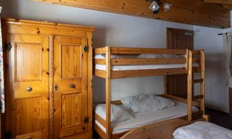A cozy bedroom with a wooden loft bed and a large wardrobe. The walls are light, and the room feels welcoming.