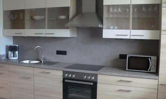 A modern kitchen with light wood furniture and glass fronts. It features a stove, a microwave, and a sink.