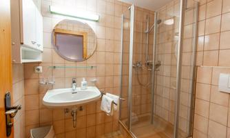 A modern bathroom with a shower and a sink. The walls are lightly tiled and there is a round mirror.