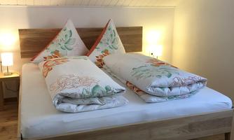 A cozy bedroom with a large wooden bed and colorful pillows. The walls are bright, and there is soft light from the bedside lamps.