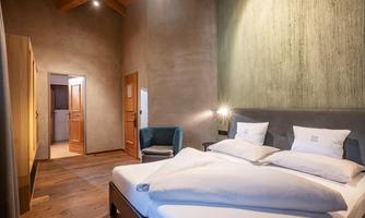 A modern bedroom with a large bed and a comfortable armchair. The warm wood tones and stylish lighting create an inviting atmosphere.